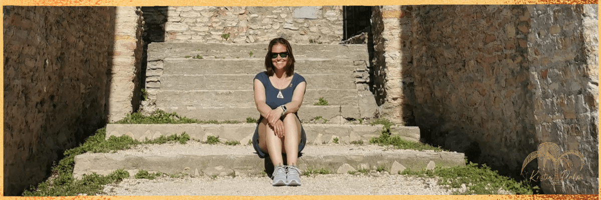 Hier siehst du Kristin Palm, Sie sitz in einem alten, mittelalterlichen und verlassenen Treppenaufgang. Die Sonne und Kristin Palm strahlen um die Wette. Sie ist dein Gesundheitsprofi für deinen Beckenboden und deine Kaiserschnittnarbe.