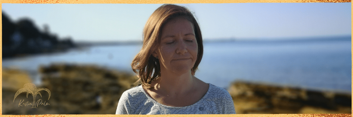 Hier siehst du Kristin Palm. Dein Profi für Beckenboden und Kaiserschnitt Behandlungen. Sie steht zufrieden und tiefenentspannt am Strand mit geschlossenen Augen und genießt den sonnigen Moment.