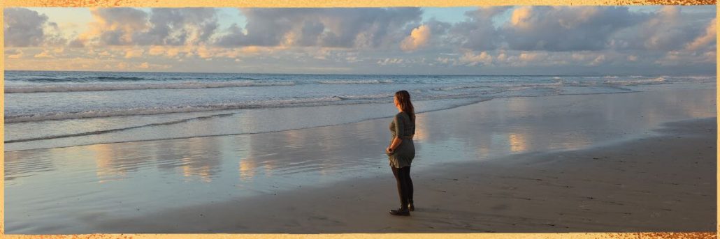 Hier ist Kristin Palm zu sehen, die über ihre langjährige Arbeit als Physiotherapeutin, ihre Leidenschaft für Yoga und Meditation sowie ihre heutige Tätigkeit als Spiritual Life Coach spricht und ihre Mission beschreibt, Menschen zu mehr Kraft, Balance und innerer Stärke zu begleiten.“ Hier steht Kristin am Strand von San Diego bei Sonnenuntergang.